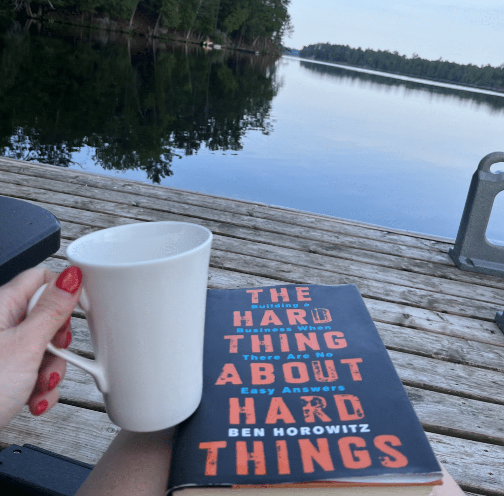 a Productive Shop employee is by the lake, reading the book The Hard Thing about Hard Things during the company's cottage retreat